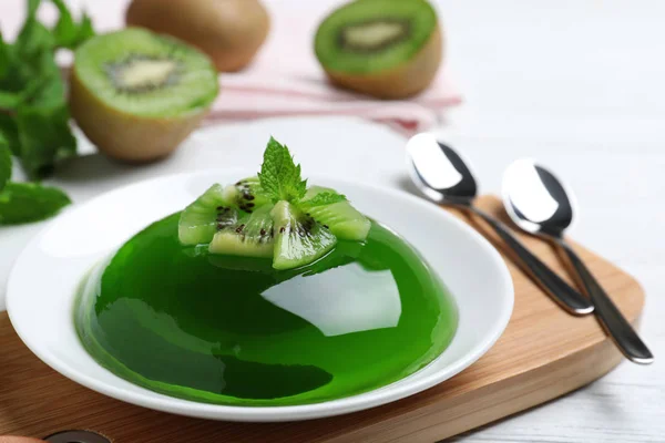 Delicious green jelly with kiwi slices on white wooden table