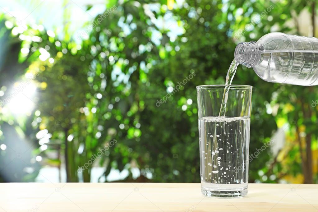 Pouring water from bottle into glass against blurred background, space for text. Refreshing drink