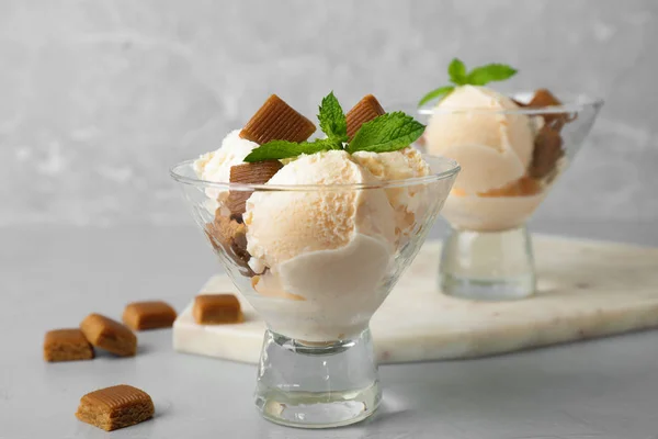 Piatto di vetro di delizioso gelato con caramelle caramello e menta sulla tavola grigio chiaro — Foto Stock