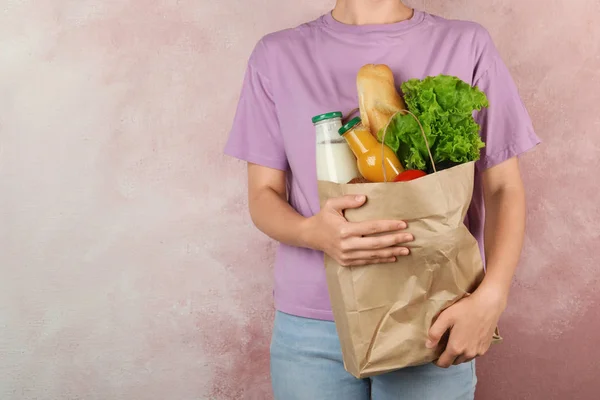 Mujer sosteniendo bolsa de papel con diferentes comestibles sobre fondo rosa. Espacio para texto — Foto de Stock