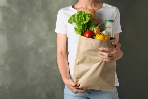 Mujer sosteniendo bolsa de papel con diferentes comestibles sobre fondo gris. Espacio para texto — Foto de Stock