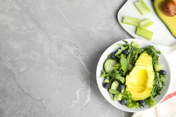 Heerlijke avocado salade met bosbessen in kom op een grijze marmeren tafel, platte lag. Ruimte voor tekst — Stockfoto
