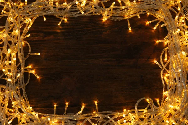 Rahmen aus leuchtenden Weihnachtslichtern auf Holzgrund, Draufsicht. Raum für Text — Stockfoto
