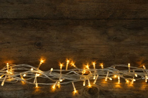 Leuchtende Weihnachtsbeleuchtung auf hölzernem Hintergrund, Draufsicht. Raum für Text — Stockfoto