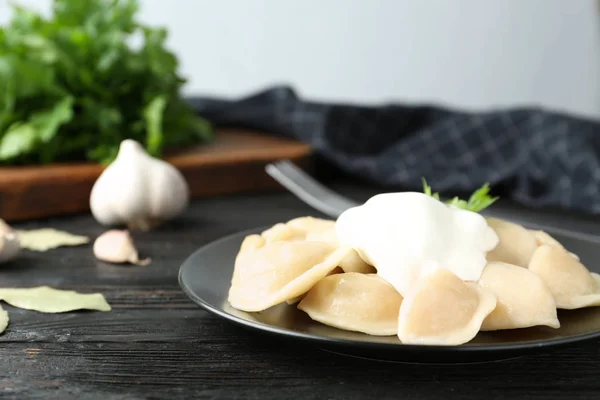 Heerlijke gekookte dumplings met zure room op donkere houten tafel — Stockfoto