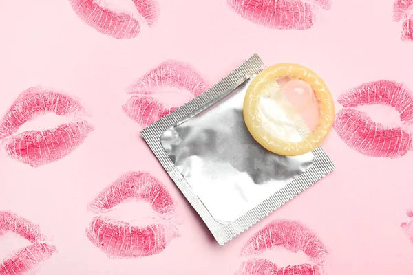 Condom with lipstick kiss marks on pink background, flat lay. Safe sex