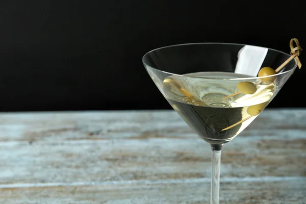 Glass of Classic Dry Martini with olives on wooden table against black background, closeup. Space for text