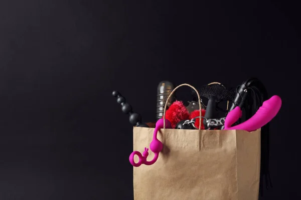 黒の背景に異なるセックスのおもちゃを持つ紙のショッピングバッグ。テキスト用のスペース — ストック写真