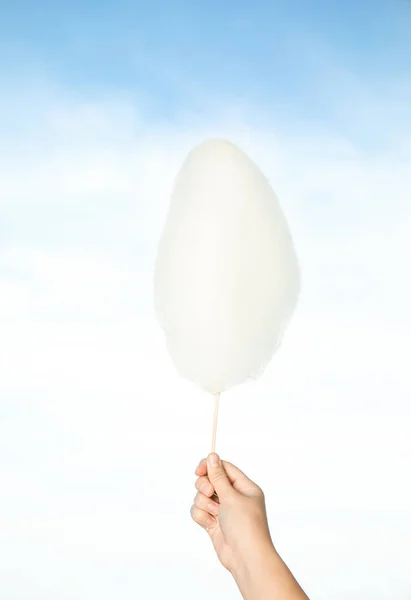 Woman holding sweet cotton candy on blue sky background, closeup view — Stock Photo, Image