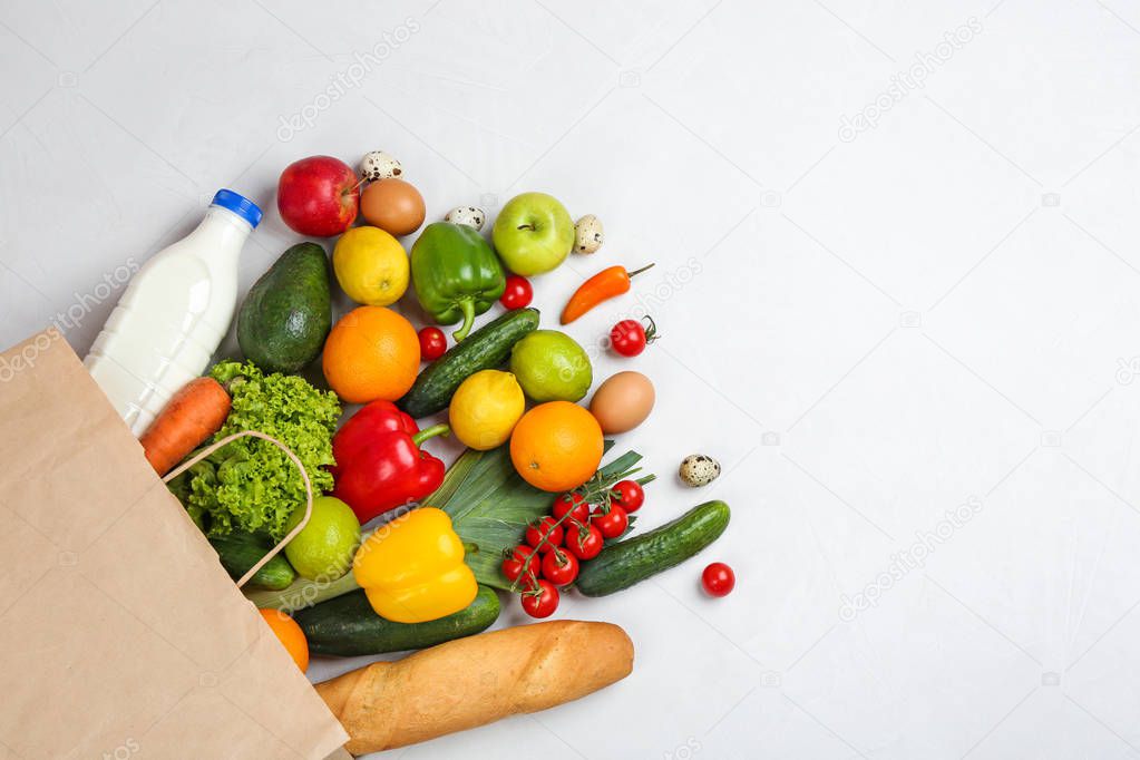 Flat lay composition with overturned paper bag and groceries on white table. Space for text
