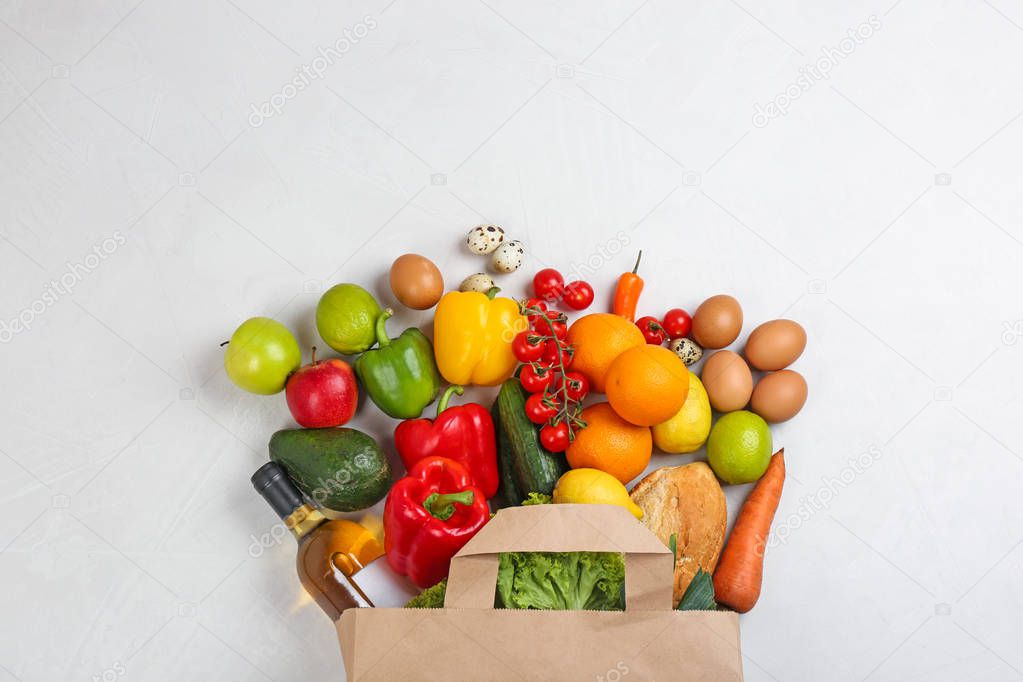 Flat lay composition with overturned paper bag and groceries on white table