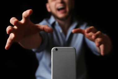Duygusal adam siyah arka plan, closeup üzerinde akıllı telefon için ulaşan. Bağımlılık kavramı