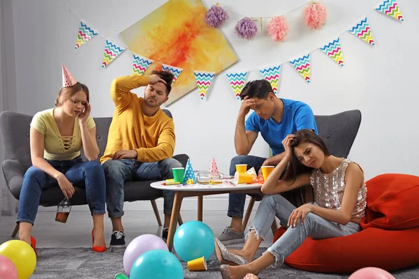 Group of friends suffering from hangover in messy room after party — Stock Photo, Image