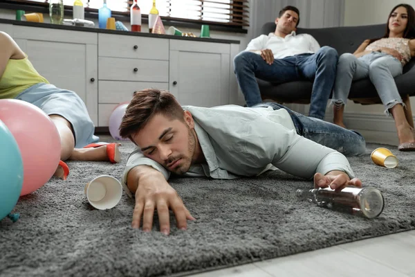 パーティーの後に乱雑な部屋で床に眠る酔っ払いの男 — ストック写真