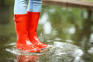 Su birikintisinde kırmızı lastik çizmeli bir kadın, yakın çekim. Yağmurlu hava