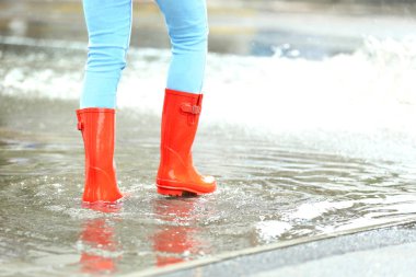 Su birikintisinde kırmızı lastik çizmeli bir kadın, yakın çekim. Yağmurlu hava