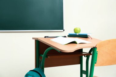 Sınıfta tebeşir tahtası yakınında kırtasiye, elma ve sırt çantası ile ahşap okul sırası