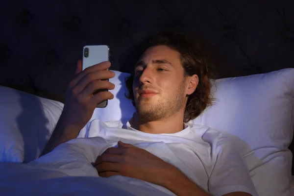 Красивый молодой человек, использующий смартфон в темной комнате ночью. Время спать — стоковое фото