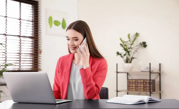 Giovane donna d'affari che parla al telefono mentre utilizza il computer portatile a tavola in ufficio — Foto Stock