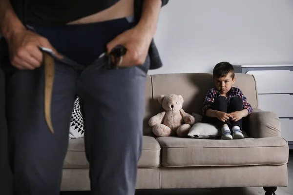 Homem com calças desapertadas perto do menino assustado no sofá dentro de casa. Criança em perigo — Fotografia de Stock