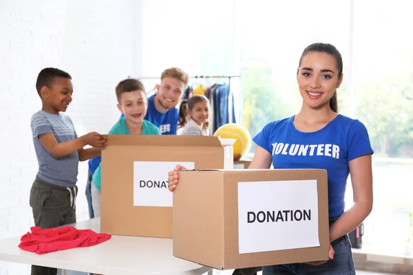 Волонтери з дітьми сортують товари пожертвування в приміщенні — стокове фото