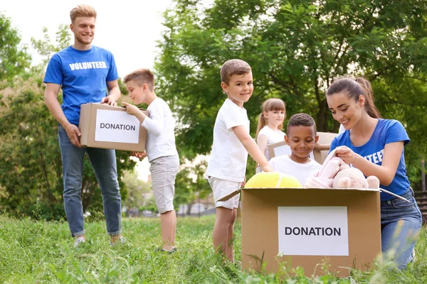 Voluntários e crianças com caixas de doação no parque — Fotografia de Stock