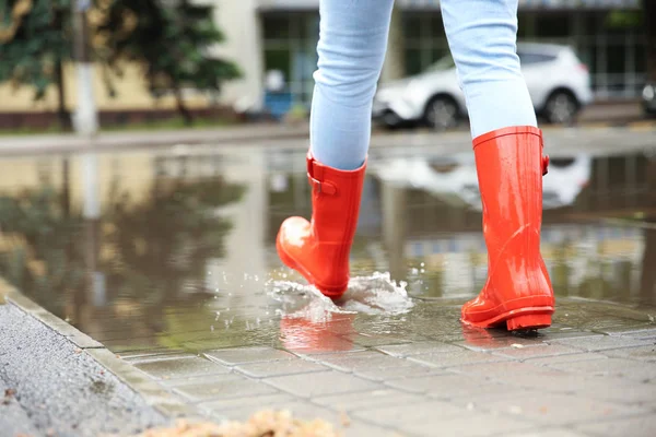 Woman with red rubber boots in puddle, closeup. Rainy weather