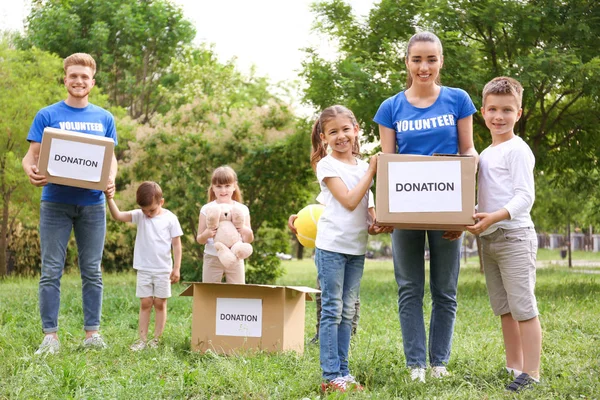 Freiwillige und Kinder mit Spendenboxen im Park — Stockfoto