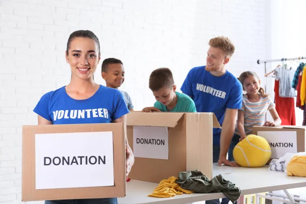 Voluntarios con niños clasificando bienes de donación en interiores —  Fotos de Stock