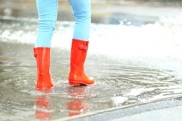Su birikintisinde kırmızı lastik çizmeli bir kadın, yakın çekim. Yağmurlu hava — Stok fotoğraf