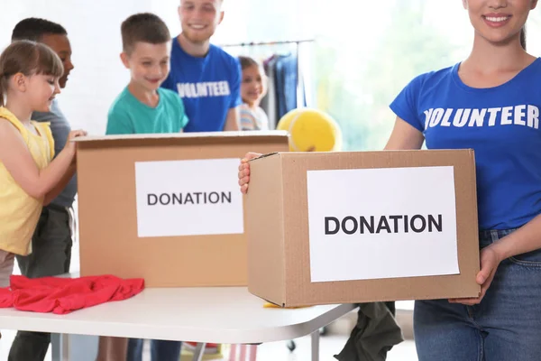 Voluntarios con niños clasificando bienes de donación en interiores —  Fotos de Stock