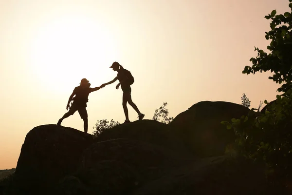 Silhouetten van man en vrouw elkaar helpen om te klimmen op de heuvel tegen zonsondergang — Stockfoto