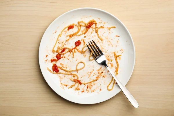 Dirty plate with food leftovers and fork on wooden background, top view — Stock Photo, Image