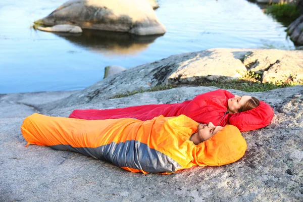 Νεαρό ζευγάρι αναπαύεται σε υπνόσακους σε γκρεμό κοντά στη λίμνη — Φωτογραφία Αρχείου