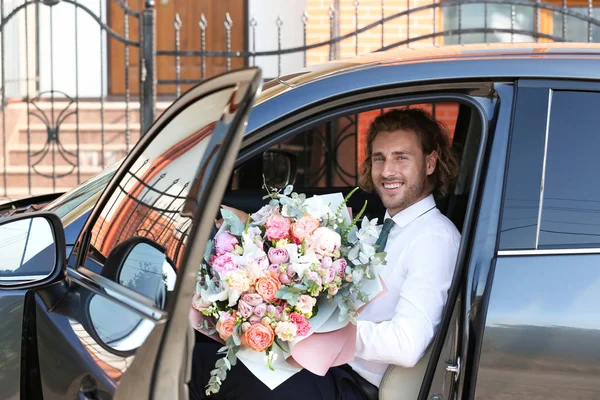 Молодой красивый мужчина с красивым цветочным букетом в машине — стоковое фото