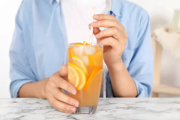 大理石のテーブルでオレンジのさわやかな飲み物のグラスを持つ女性, クローズアップ — ストック写真