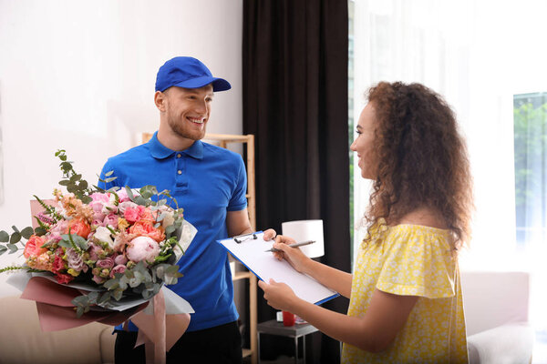 African-American woman receiving flower bouquet from delivery man indoors