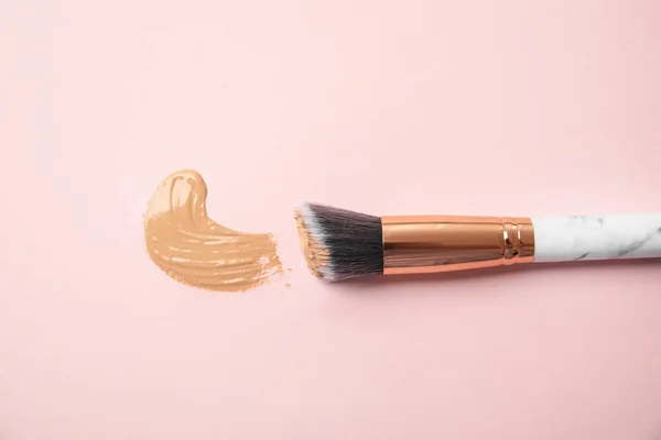 Sample of liquid foundation and makeup brush on pink background