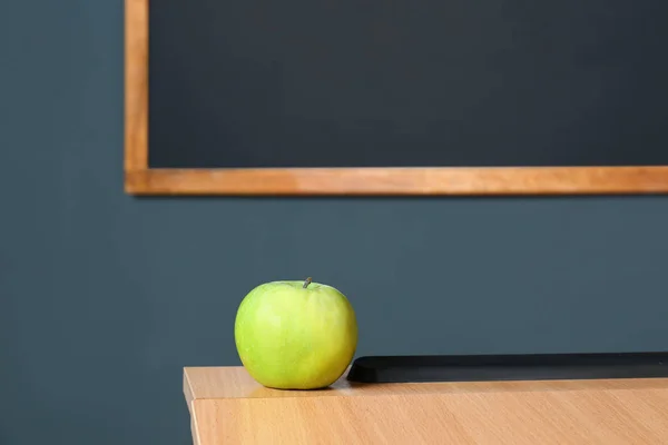 Wooden school desk and apple near blackboard on grey wall Royalty Free Stock Photos