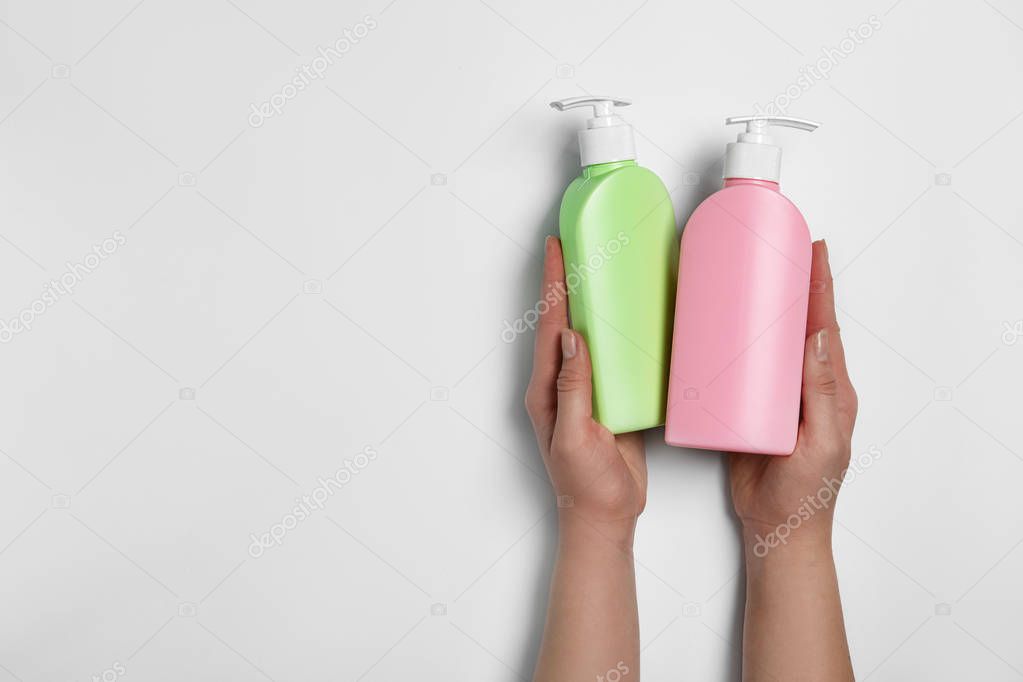 Woman holding blank bottles of cosmetic products on light background, top view. Space for design