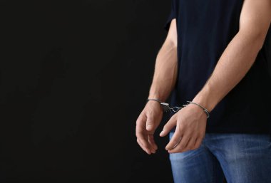Karanlık arka plana karşı kelepçeli olarak gözaltına alınan adam, mesaj için yer. Ceza hukuku