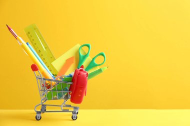 Sarı arka plan üzerinde farklı okul kırtasiye ile küçük alışveriş sepeti. Metin için alan