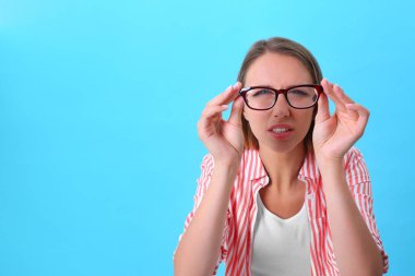 Görme sorunu olan genç kadın mavi arka planda gözlük takıyor