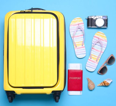 Mavi arka plan üzerinde sarı bavul ve plaj nesneleri, düz yatıyordu