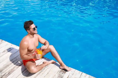 Güneşli bir günde yüzme havuzu yakınında ferahlatıcı kokteyl ile yakışıklı genç adam. Metin için alan