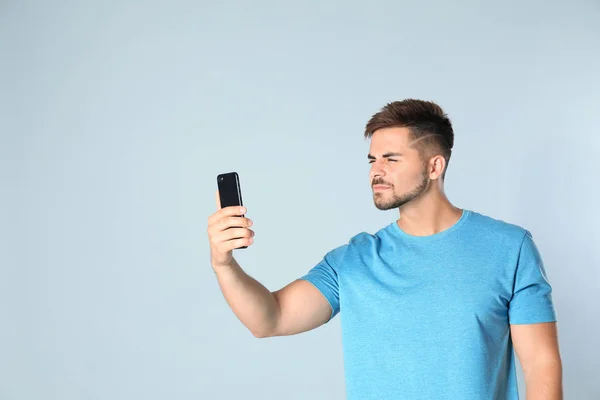 Young man with vision problems using smartphone on grey background, space for text — Stock Photo, Image