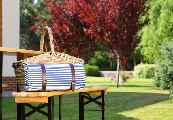 Picknickmand met deken op houten bankje in de buurt van de tafel in de groene tuin — Stockfoto
