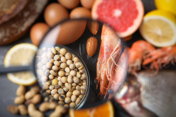 Different products with magnifier focused on soy beans and shrimps, closeup. Food allergy concept — Stock Photo, Image