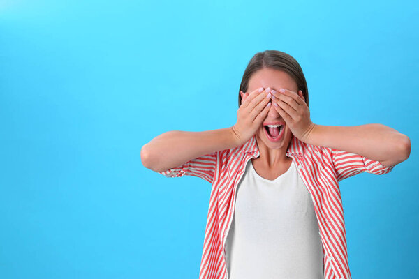 Young woman covering eyes with hands on blue background. Space for text