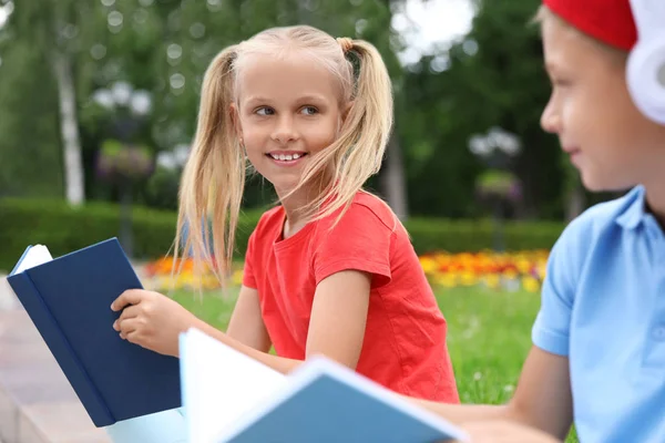 Lindo chico en auriculares y niña leyendo libros en el parque verde —  Fotos de Stock